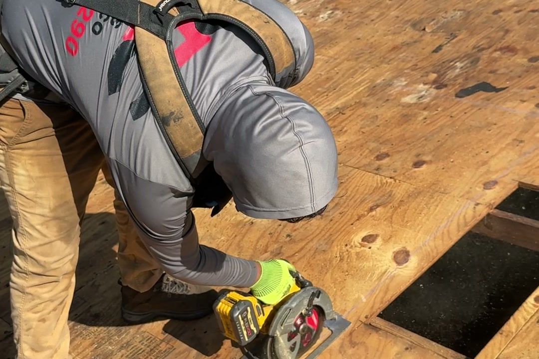 Roofer cutting a section of rotted plywood out of a roof deck with a circular saw