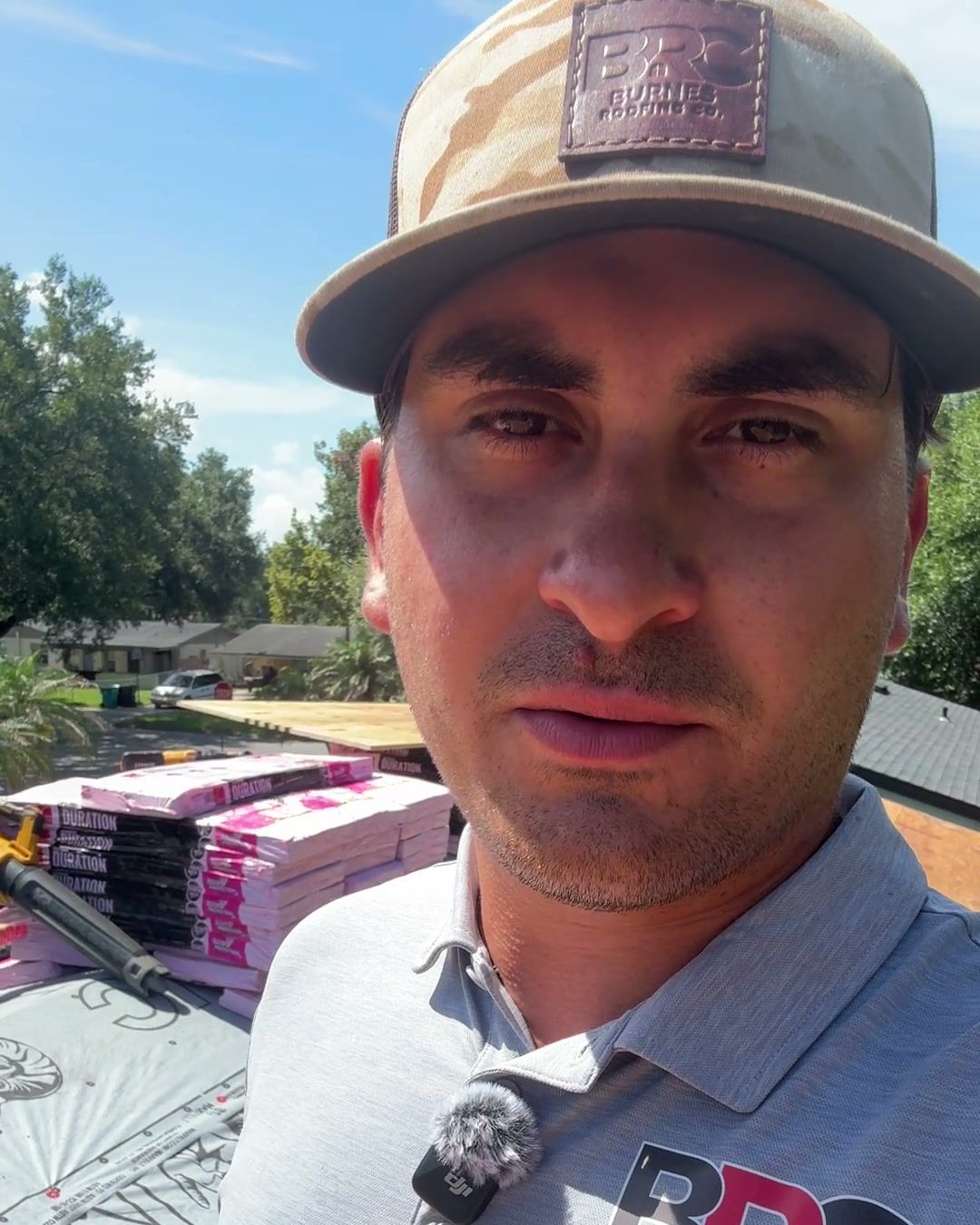 Tommy Burnes, owner of Burnes Roofing Company, on a roof during a re-roof with shingle bundles behind him